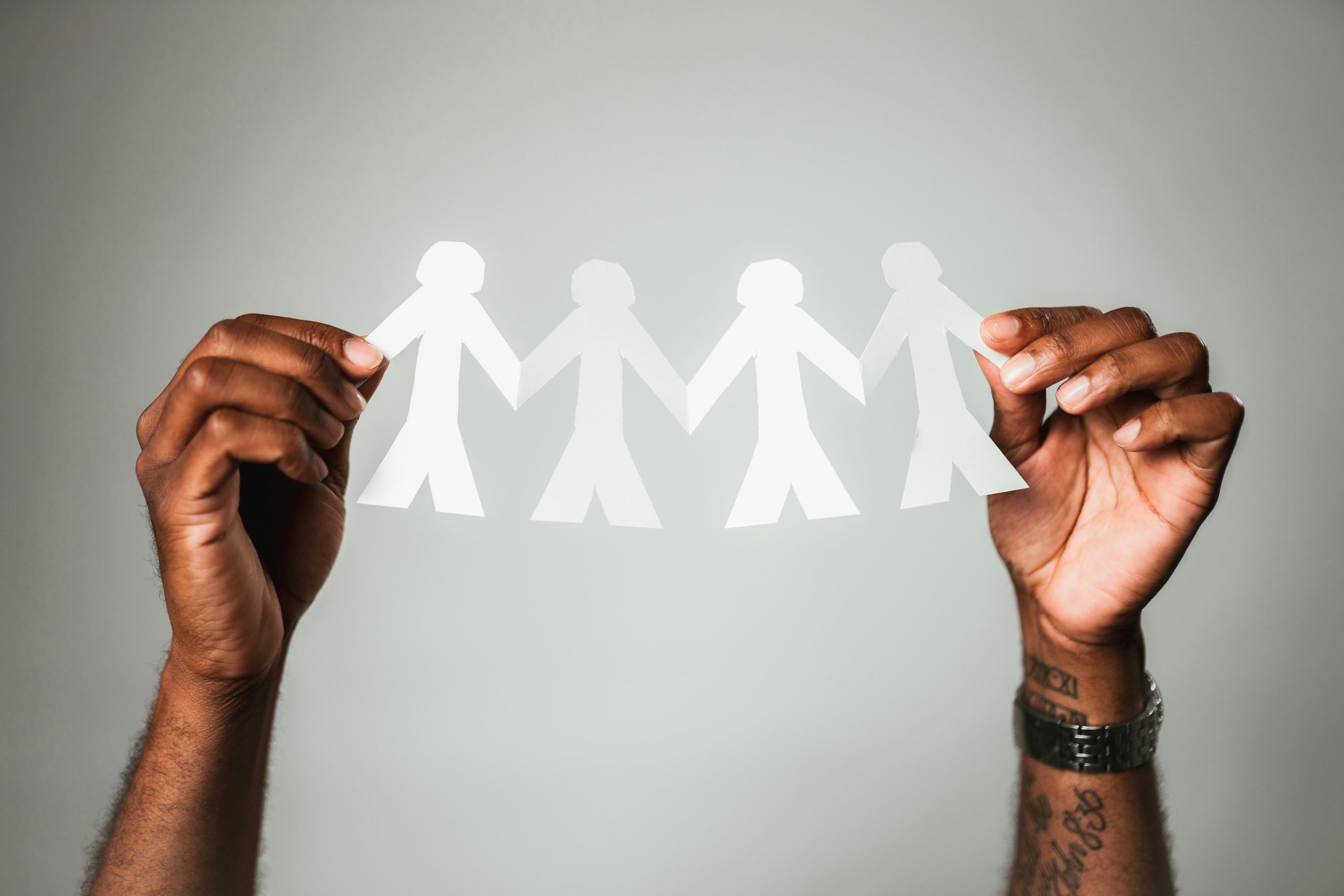 Hands holding a paper cutout of four connected figures against a plain background.
